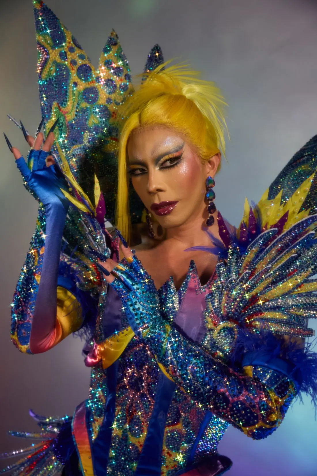 A Heals queen in a yellow wig and a jewelled coral costume