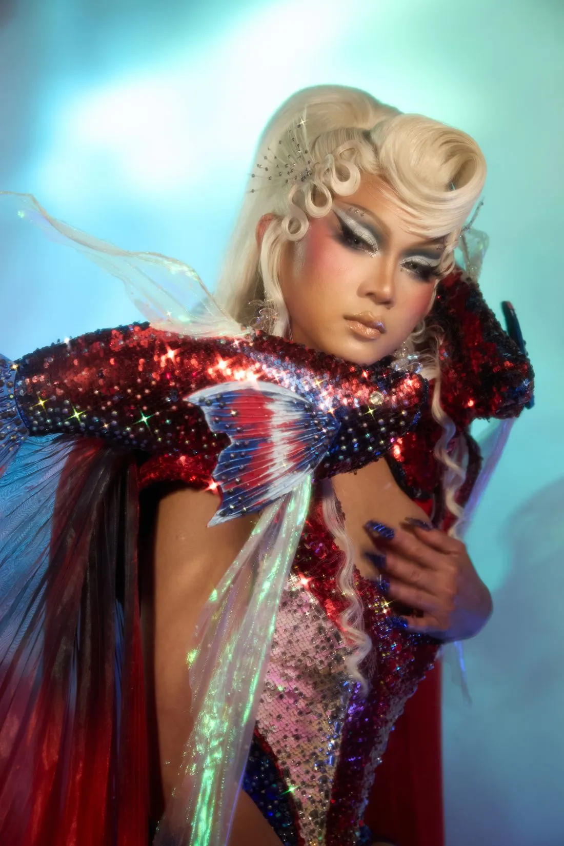 A Heals queen in platinum curls and a red sequinned fish-fin costume